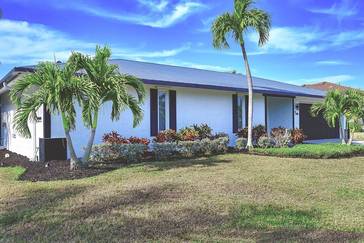 Single-story Marco Island home with a metal roof, palms and tropical landscaping out front